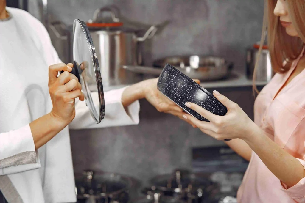 Two shoppers comparing an enameled aluminum saucepan with glass lid in a kitchenware store