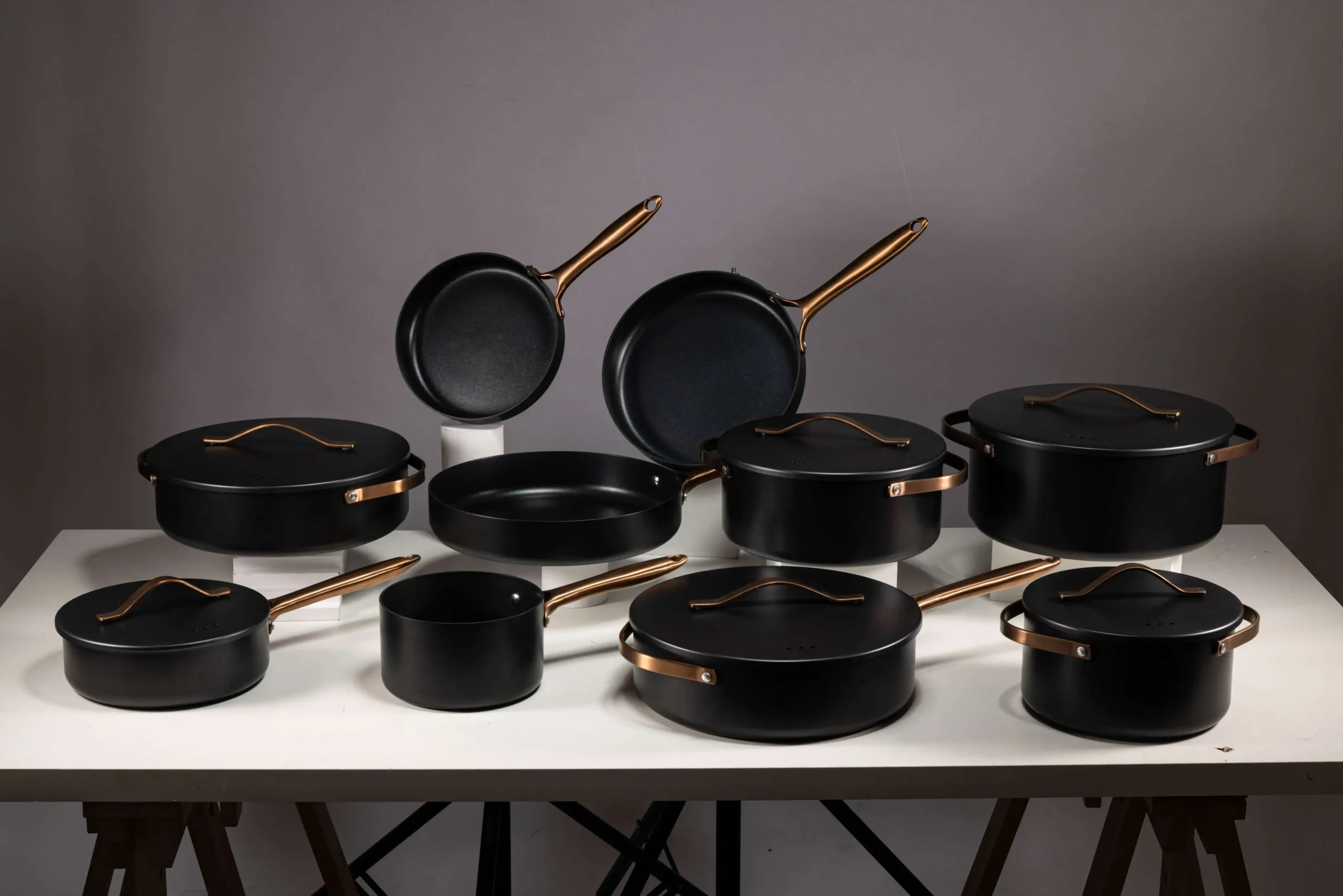 Modern aluminum cookware set with gold handles displayed on a white table, perfect for contemporary kitchen aesthetics