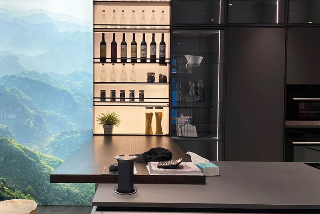 Eine moderne Küche mit eleganten schwarzen Schränken und einem Holztisch, der aus der Insel herausragt, mit malerischem Bergblick durch das Fenster