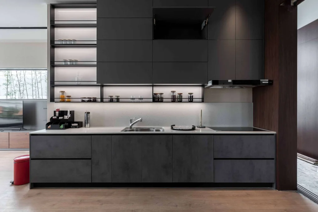 Eine stilvolle Küche mit mattschwarzen Schränken, einer Dunstabzugshaube aus Edelstahl und einer dunklen Arbeitsplatte mit einem Blick auf einen Wohnbereich im Hintergrund
