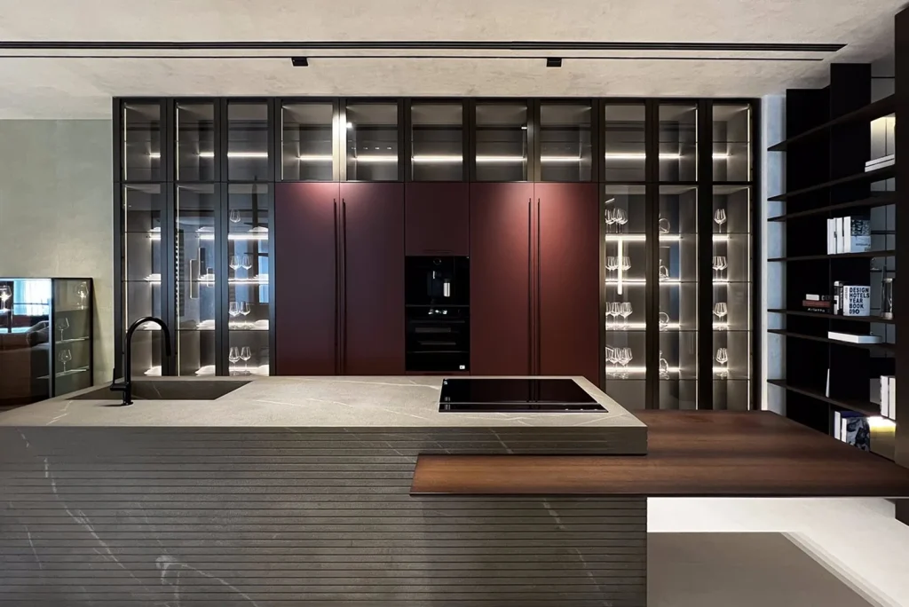 Eine großzügige, moderne Küche mit einer großen Insel aus dunklem Holz, passenden Schränken und integrierter Beleuchtung, die Glaswaren und Bücher in den Vordergrund stellt